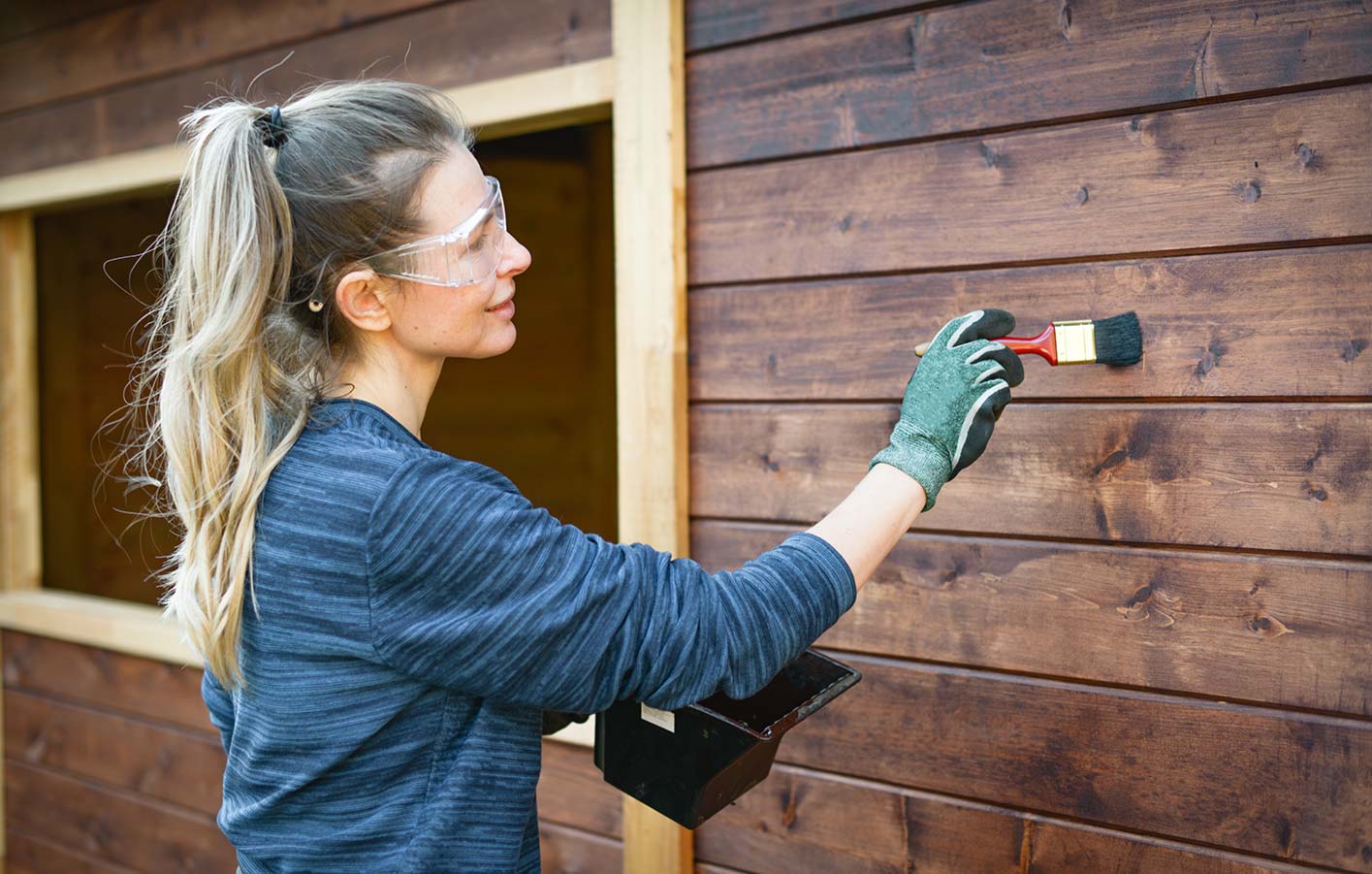 Frau streicht Fassade vom Holzhaus